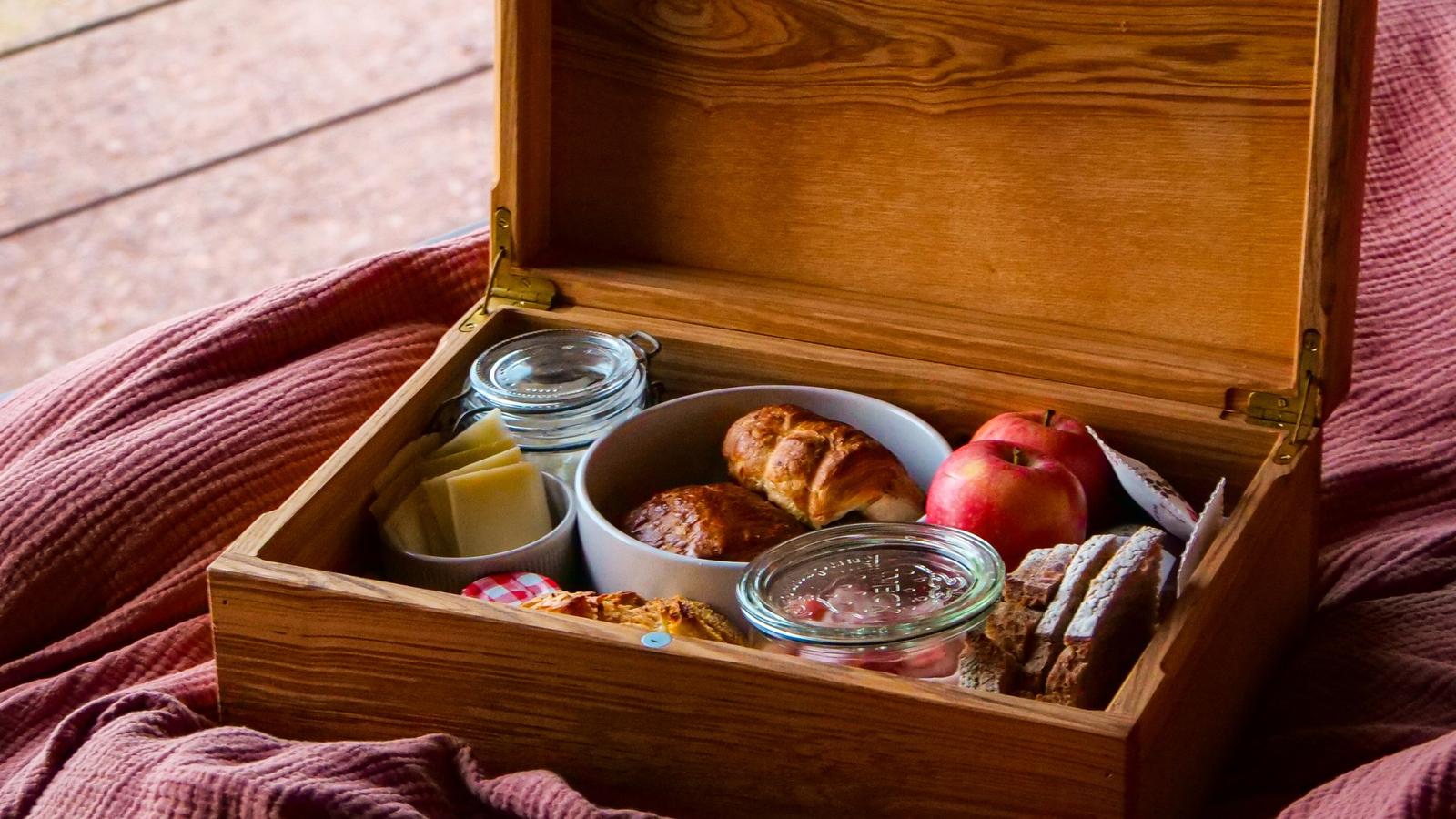 Coffret en bois du petit-déjeuner posé sur le lit : viennoiseries, pommes, fromage et confitures