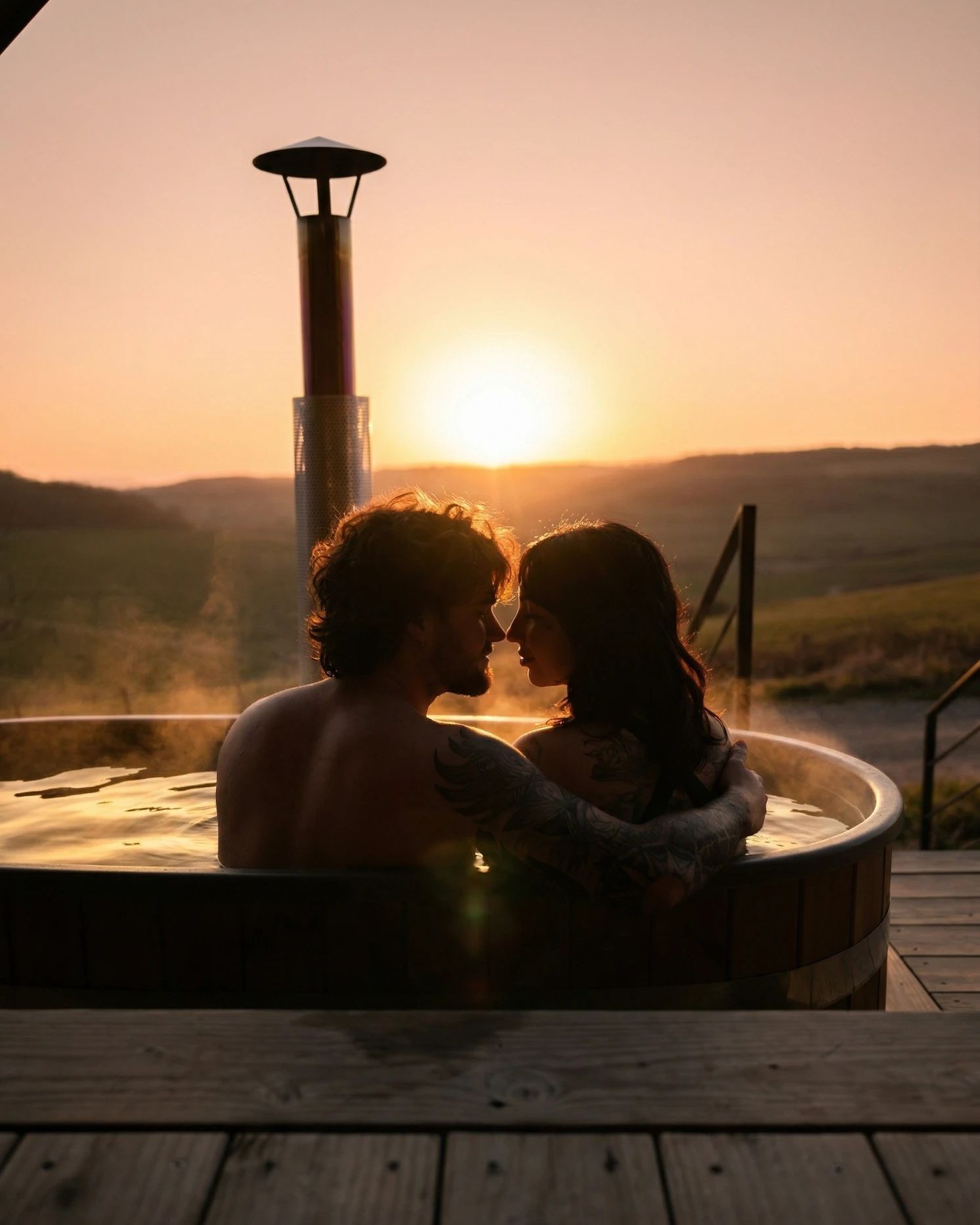 Un couple enlacé dans le bain nordique au coucher du soleil, face à la vallée