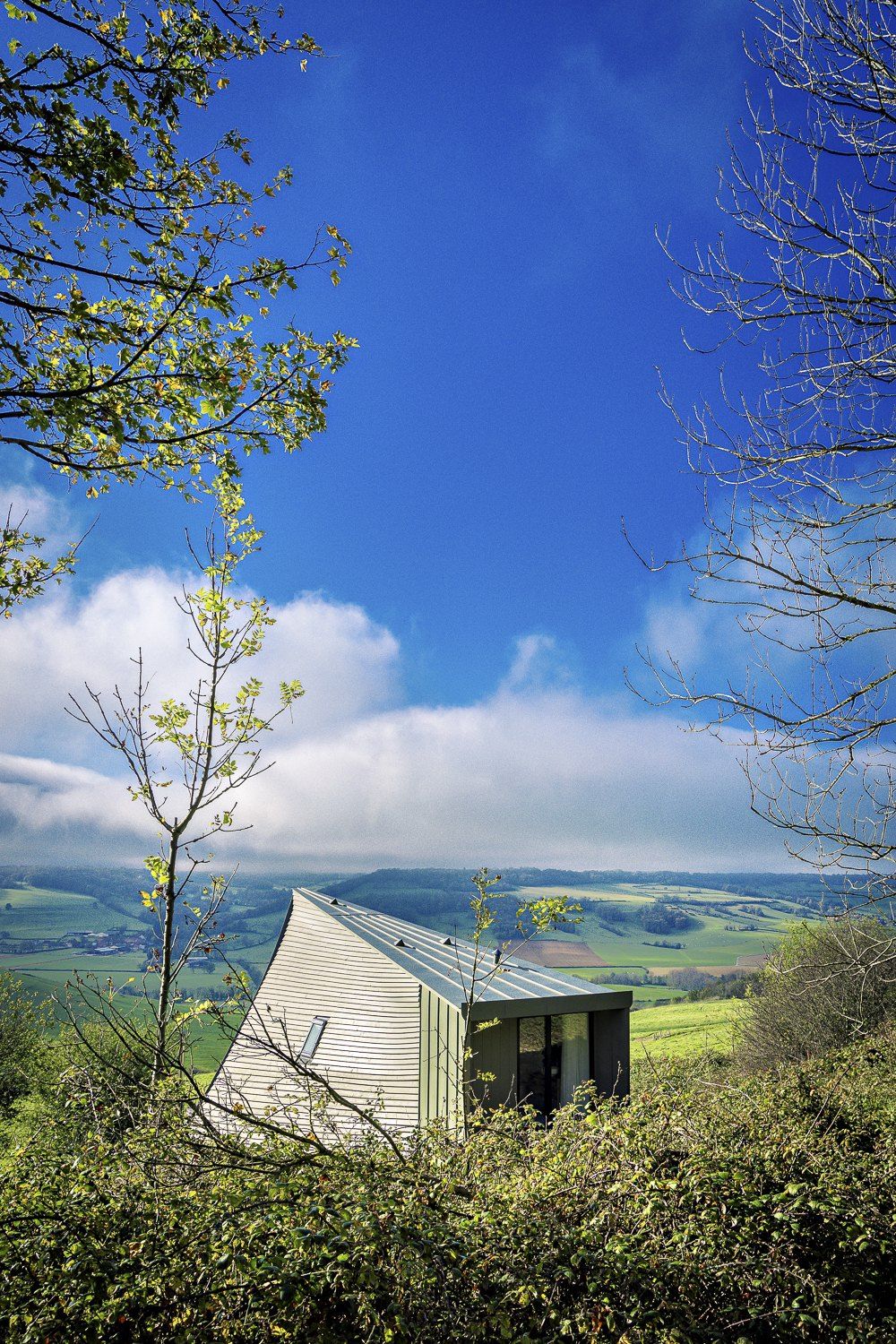 Un lodge au bardage clair dans la verdure, face à la vallée sous un ciel bleu