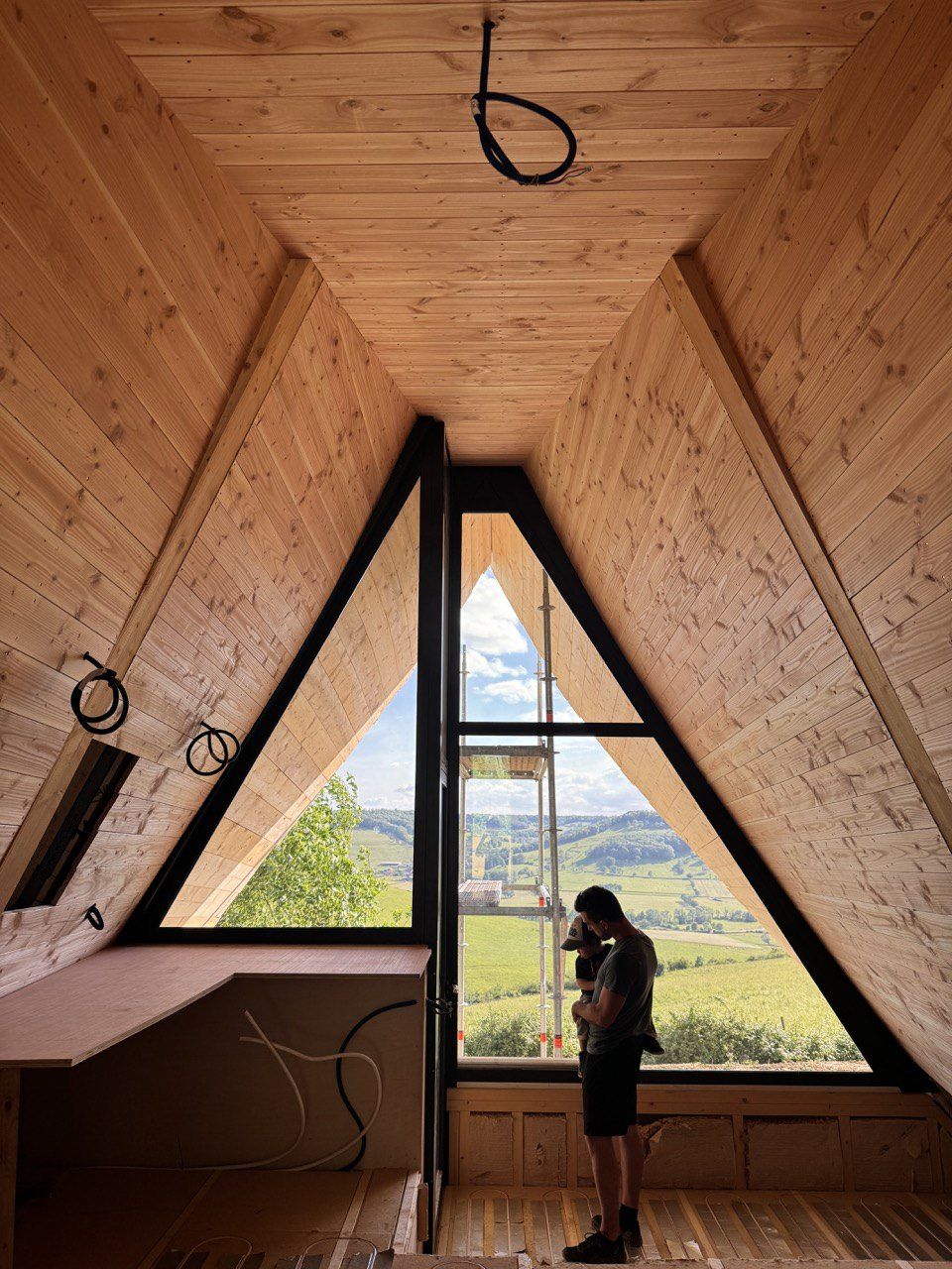Intérieur d’un lodge en bois brut, la grande baie ouverte sur la nature