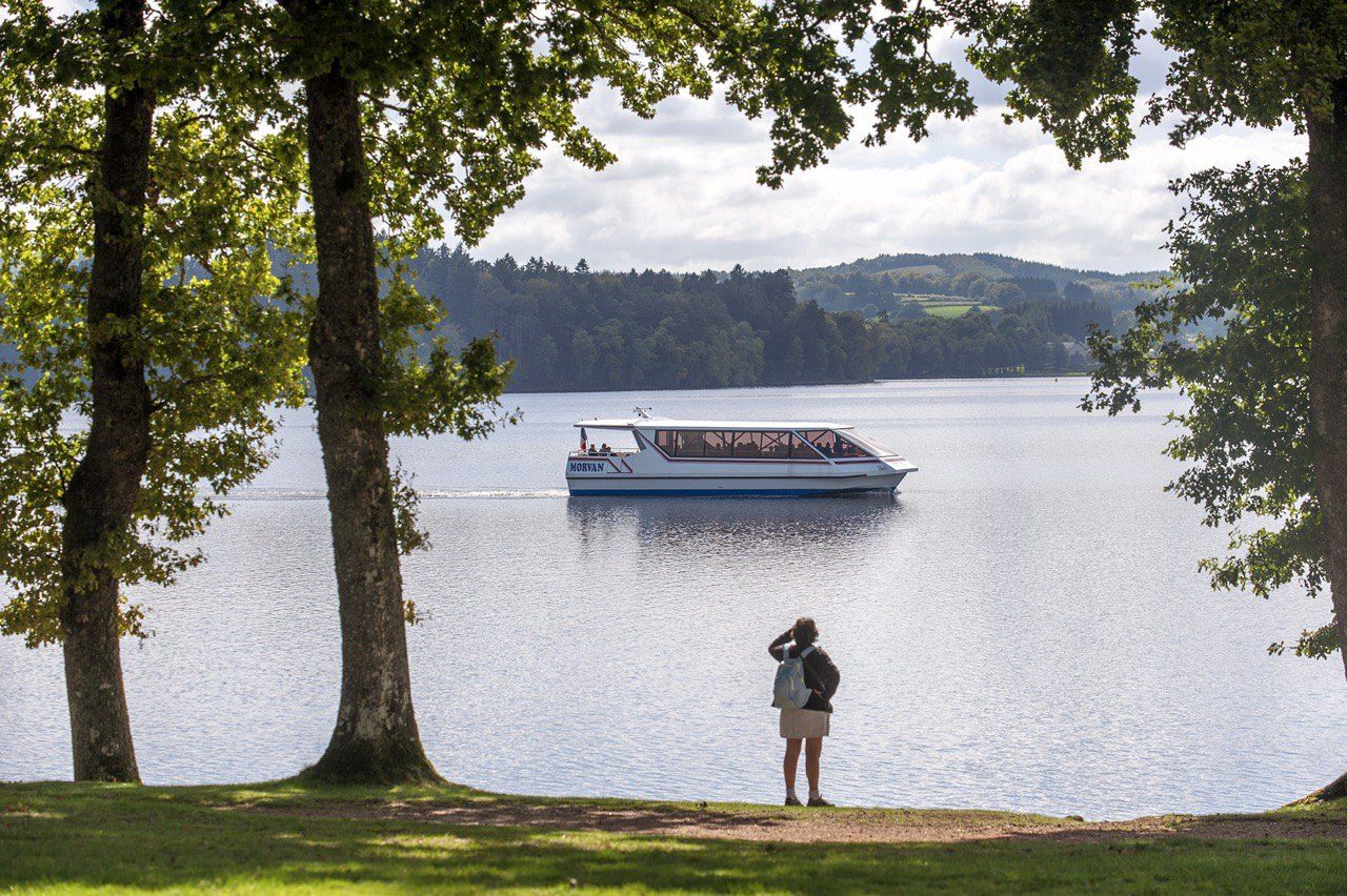 Lac du Morvan entouré de collines boisées, avec un bateau et un promeneur