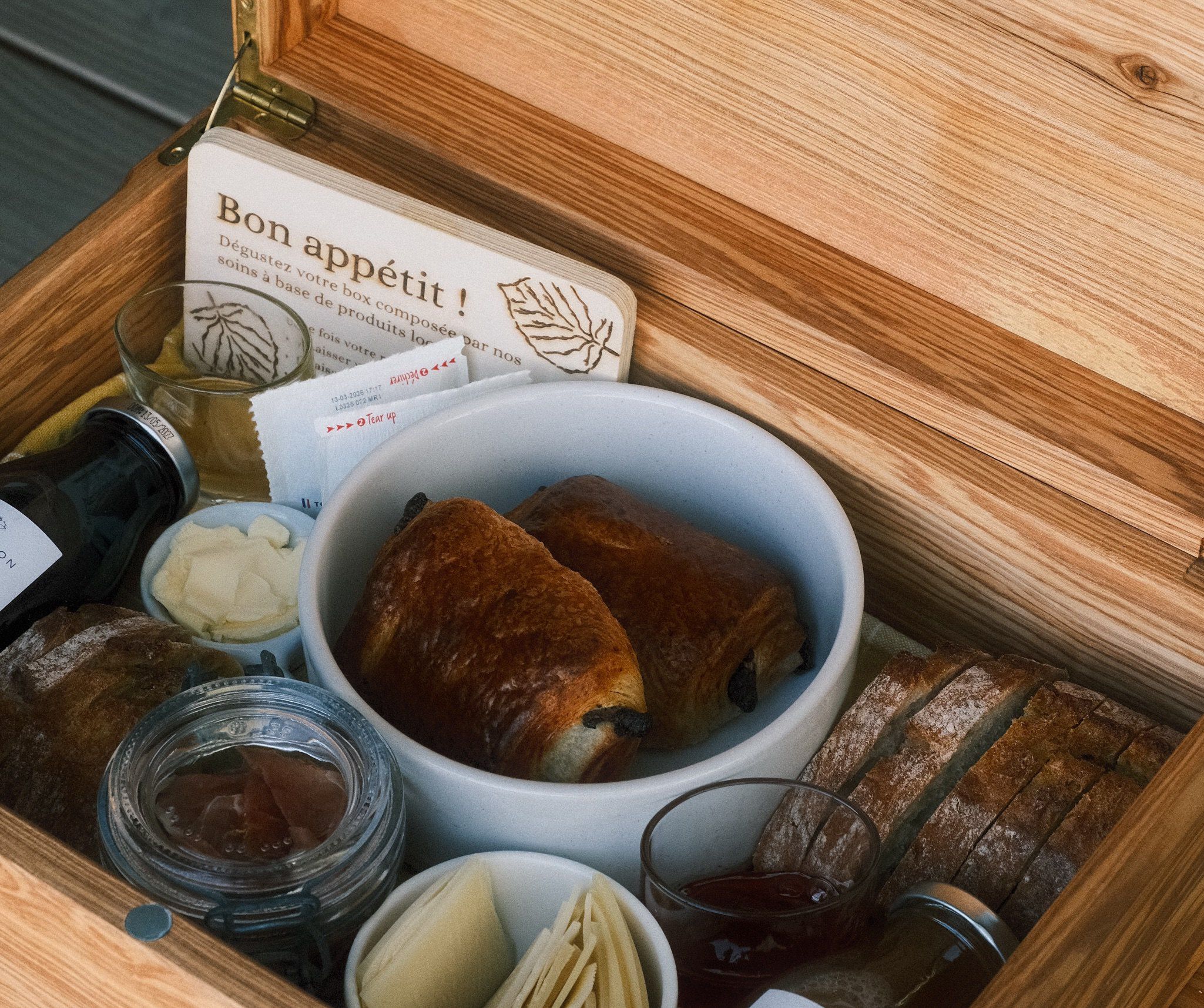 Panier de petit-déjeuner en bois avec viennoiseries, confitures et fromage