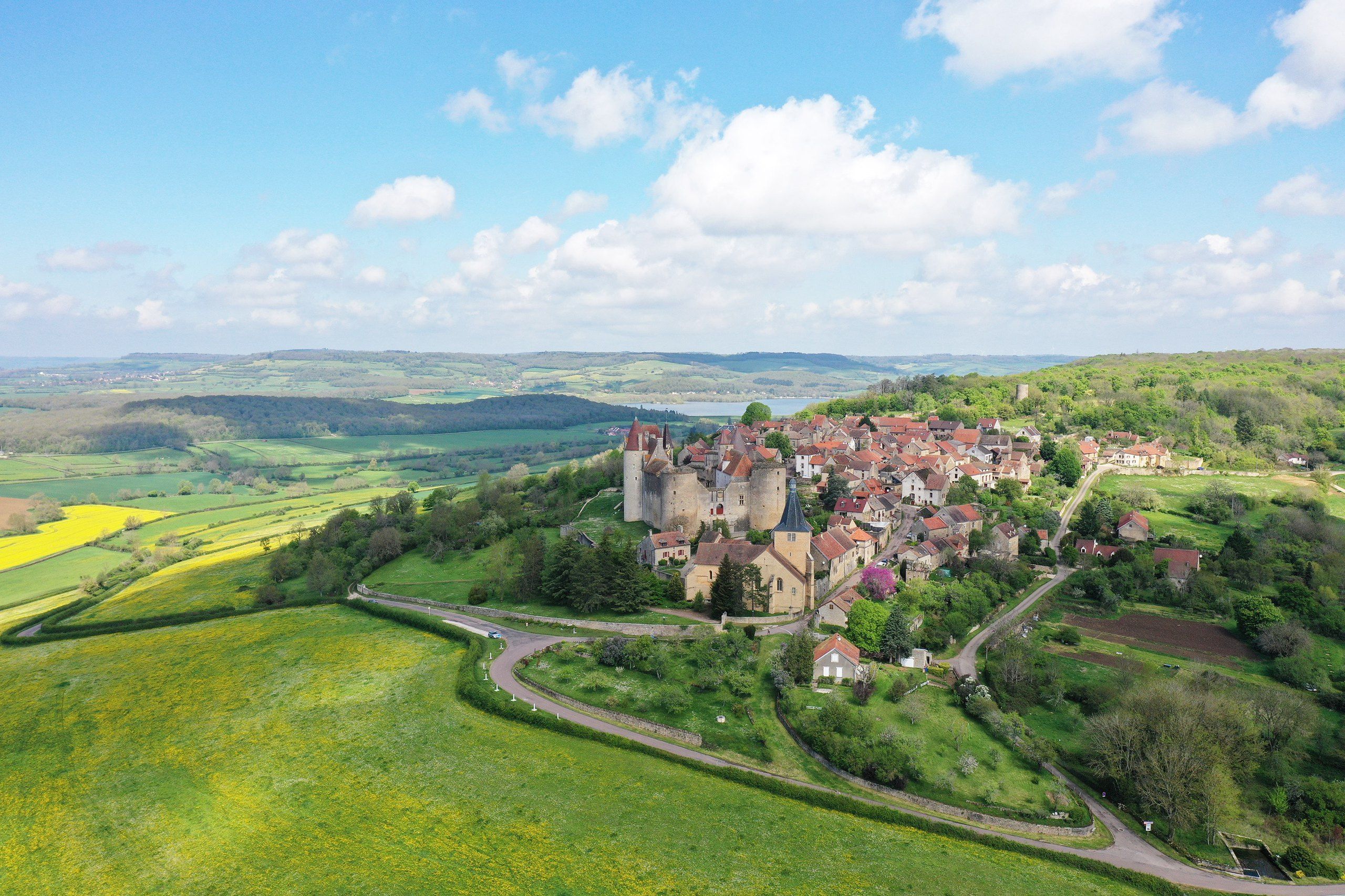 Village médiéval perché sur une colline et entouré de verdure, vu du ciel