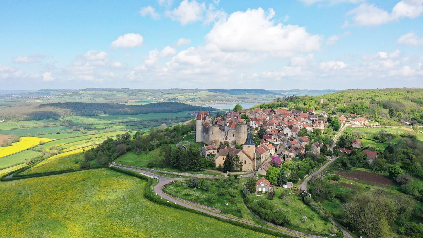 Village médiéval perché sur une colline et entouré de verdure, vu du ciel